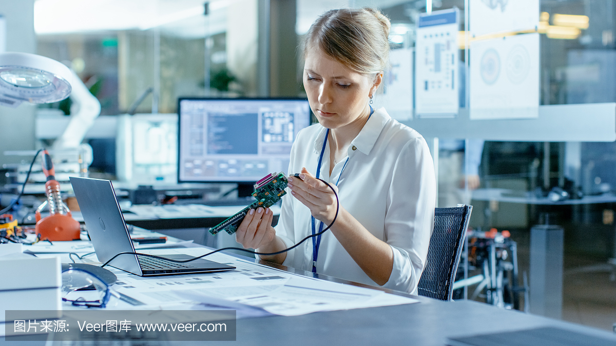 女計算機科學家將電路板連接到她的筆記本電腦并開始編程。她在先進技術實驗室工作。